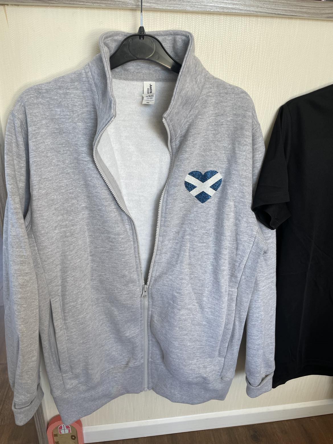 a photo of a grey zipped jacket showing the heart shaped saltire in glitter on the front pocket area